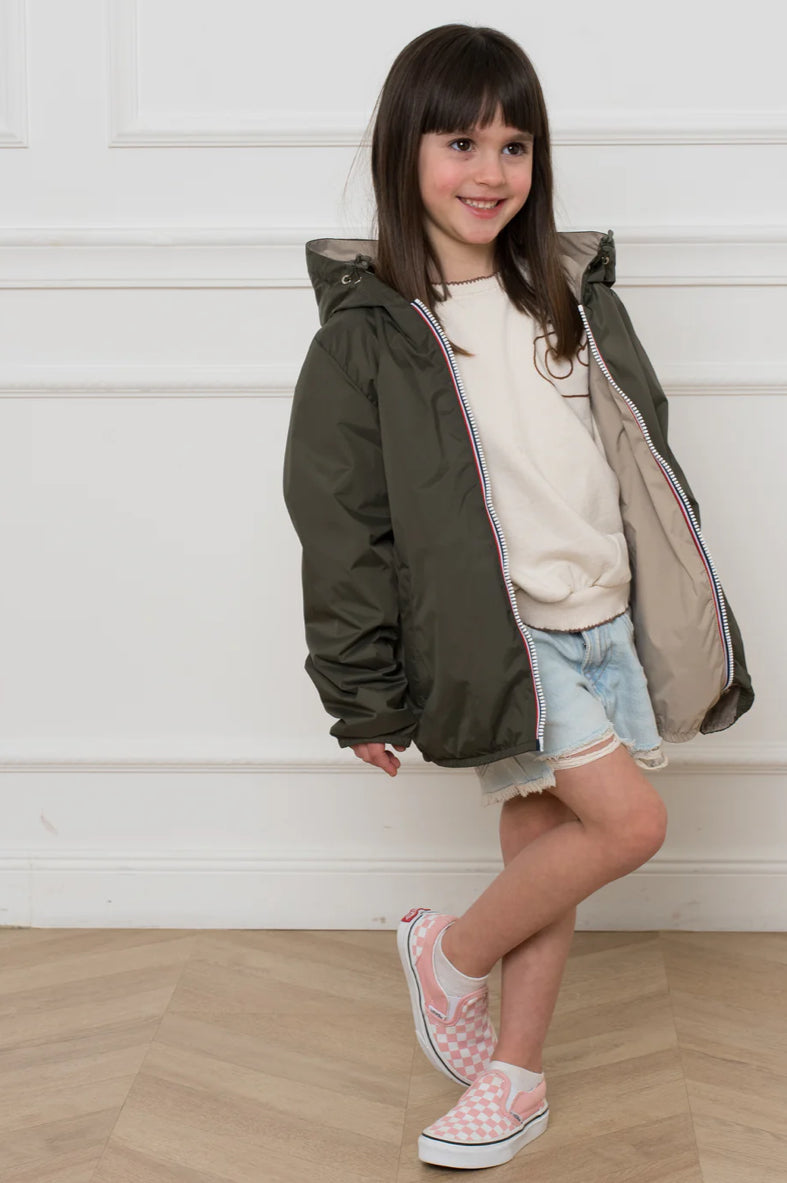Un enfant portant l'imperméable réversible léger GARANCE KIDS LAURA JO, coupe droite, capuche avec cordon et fermeture zippée, visible en extérieur.